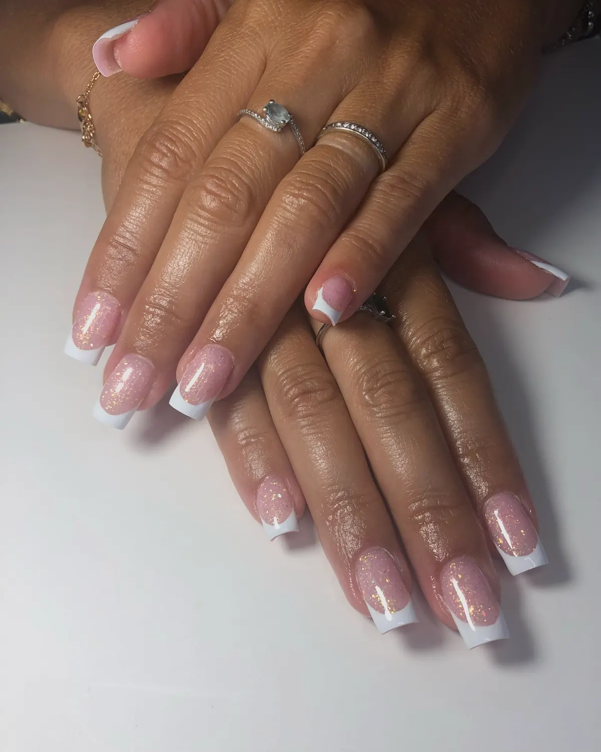 Deux mains posées l'une sur l'autre, ongles carrés en French blanche sur base rose pailletée d'or